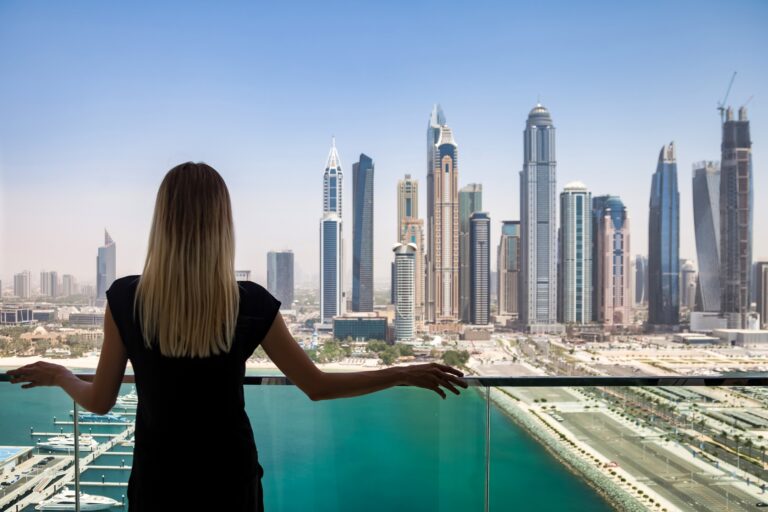 Rear view of slim woman in black attire stand on balcony, view of skyscrapers Dubai UAE